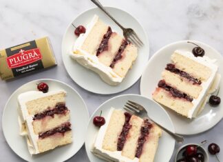 White Forest Cake Slices of cherry layer cake on white plates with whipped frosting and fresh cherries nearby; butter box in corner for context of ingredients? (informative food image)