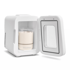 White compact beverage frother with a glass blending cup containing a light-colored smoothie or milkshake inside