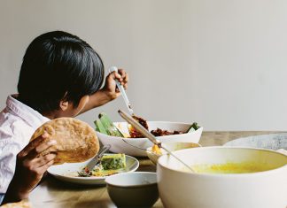 Asha Gomez’s Roti child holding roti while making a plate at the table