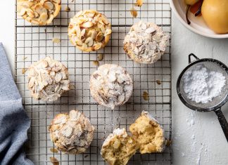 Champagne-Poached Pear Muffins A close-up view of Champagne Poached Pear Muffins beautifully arranged on a wire rack, showcasing the muffins' golden-brown tops and chunks of poached pear elegantly placed on each muffin