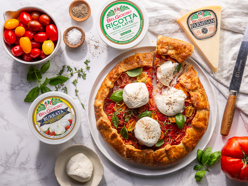  visual representation of a Three Cheese & Tomato Crostata from Bake from Scratch. The crostata is skillfully crafted, with a golden, flaky crust embracing a rich filling of three cheeses and ripe tomatoes. The dish showcases a harmonious blend of textures and colors, inviting anticipation of a delicious culinary experience