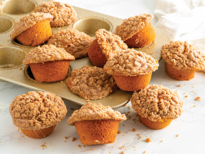 Snickerdoodle Pumpkin Muffins in GoldTouch muffin tin scattered on white surface.
