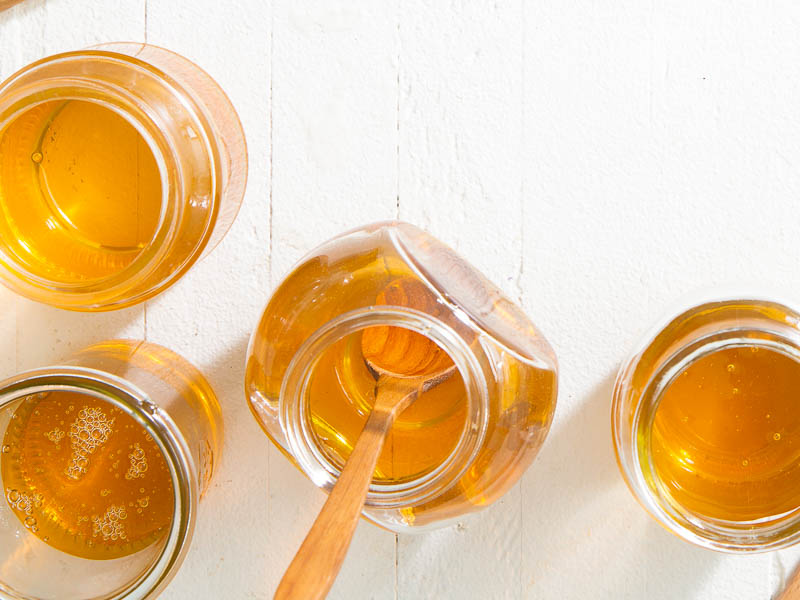 Multiple jars of honey on a counter with a honey stick in one jar