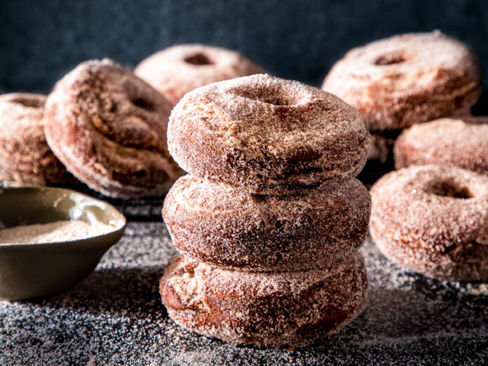 Spiced apple cider doughnuts on dark surface with cinnamon sugar spread