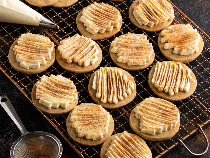 chai spice cookies with vanilla frosting topped with cinnamon on wire rack.