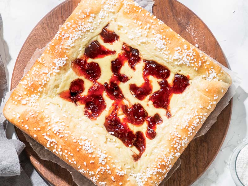 Jam and Cream Brioche Tart on Wood Trivet on Marble with Bowl of Jam with a Spoon