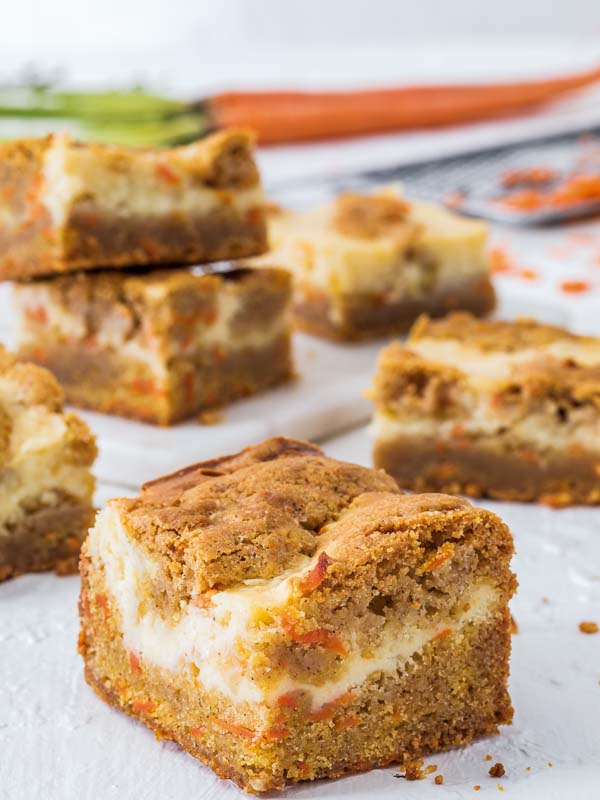 Carrot Cake Cheesecake Bars on white cutting board with carrots