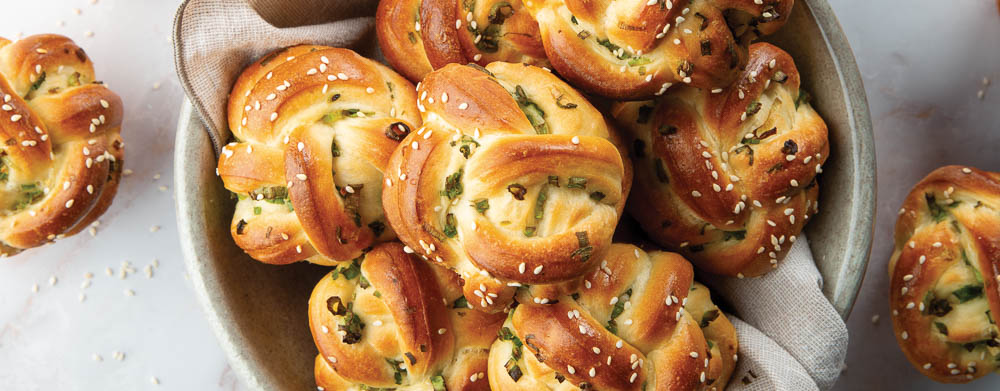 Sesame-and-Green Onion Knots in bowl with linen napkin on marble