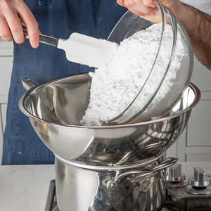 Pouring confectioners' sugar into mixing bowl over pot on stove