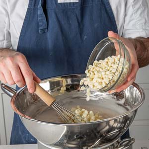 Pouring white chocolate chips into mixing bowl over pot on stove