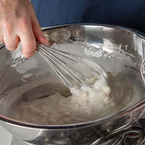 Mixing melting white chocolate chips in mixing bowl over pot on stove