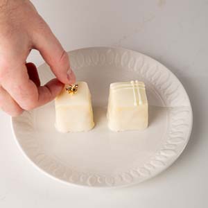 Decorating petit fours with gold leaf on white plate