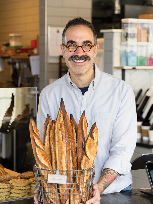 The Rise of Small State Provisions Kevin Masse with a basket of baguettes inside of Small State Provisions