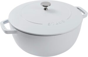 White Staub enameled cast-iron Dutch oven with matching lid and a metal knob, shown from a slight angle with two side handles visible