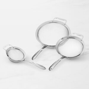 Three stainless steel mesh strainers with curved handles on a light marble surface, grayscale product photo