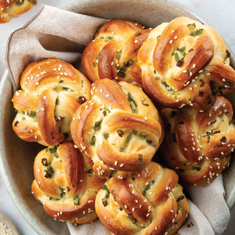 Pile of sesame-topped savory knots with chopped herbs in a basket.