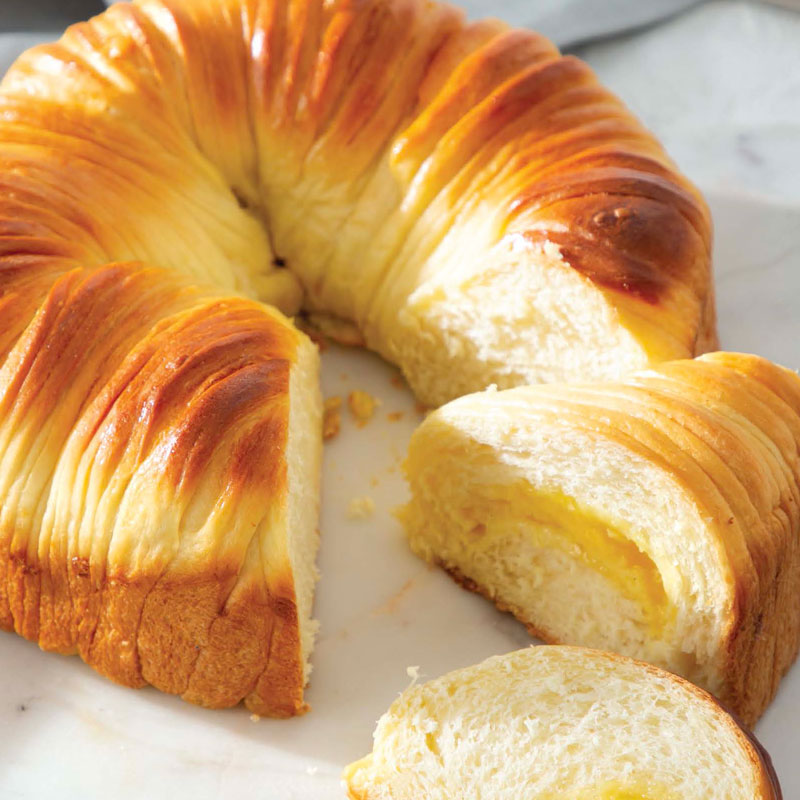 A ring-shaped braided pastry with a glossy golden crust, sliced to reveal a pale filling inside.