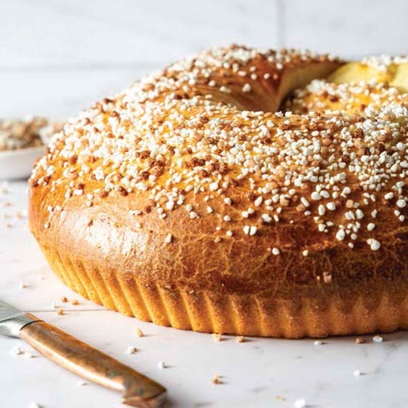 Bundt cake with pearl sugar topping on a marble surface, a knife nearby.