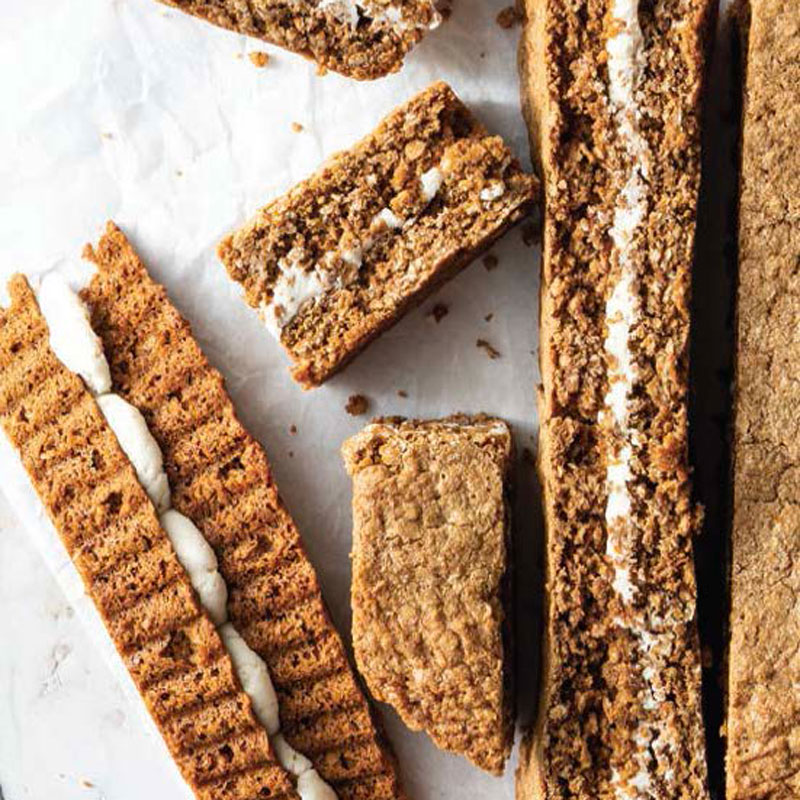 Several biscotti-style cookies with almond pieces and a white cream filling arranged on parchment.