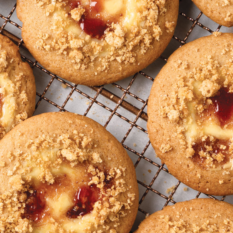 Round cookies with crumb topping and jam centers cooling on a wire rack.