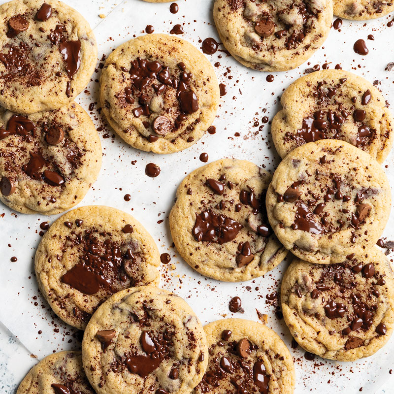 Assorted chocolate chip cookies scattered on a white surface with melted chocolate chunks.