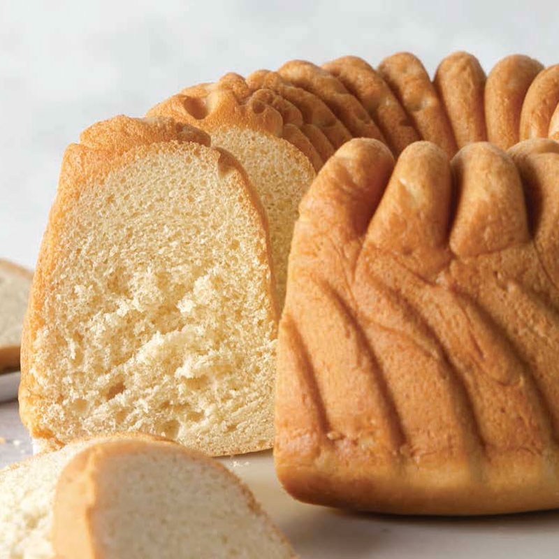Loaf of soft white bread with a decorative ridged crust, partially sliced and fanned on a light surface.