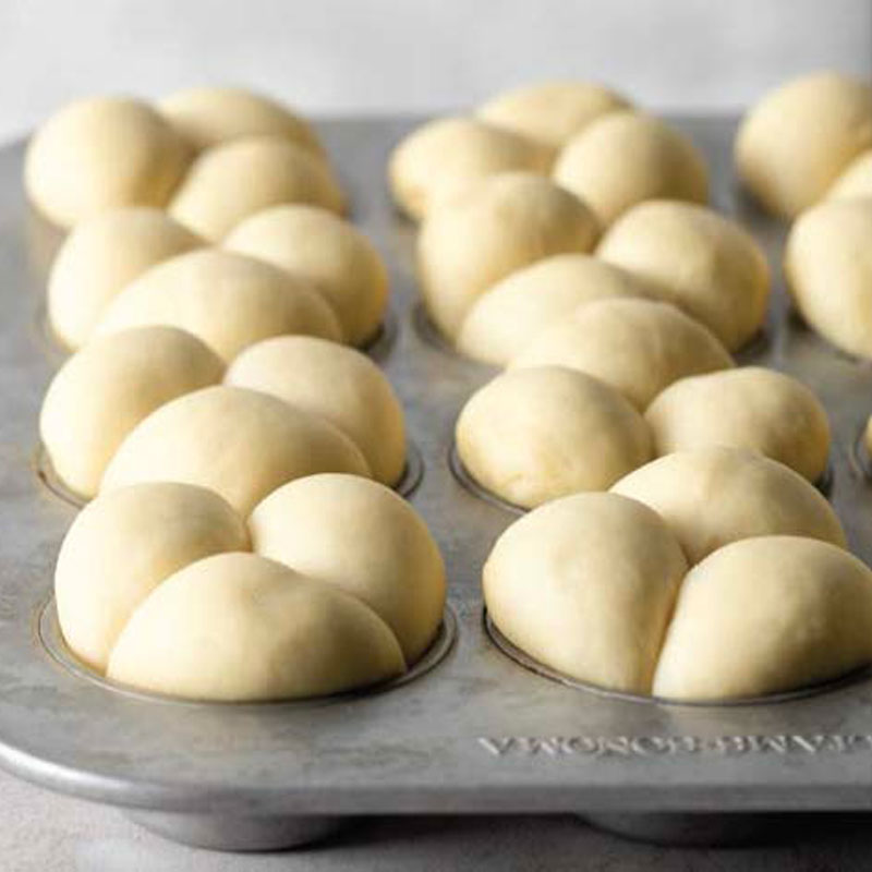 Dough balls arranged in a metal muffin pan, ready to bake on a baking sheet