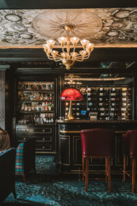 Luxurious bar with black wood cabinets, a crystal chandelier, and liquor shelves behind the counter.