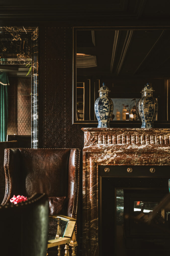 Luxurious living room corner with dark wood paneling, a marble fireplace mantle, and two blue-and-white ceramic vases, reflected in a mirror.