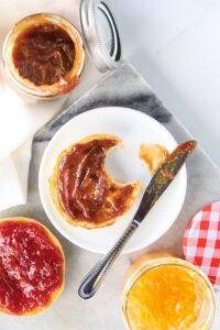 Open jar of strawberry jam with toasted bread smeared in jam on a white plate and a knife nearby on a marble countertop?
