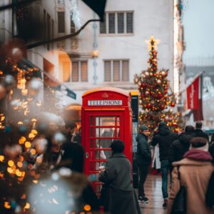 London Red British telephone booth on a bustling, festive street with a Christmas tree and string lights in the background