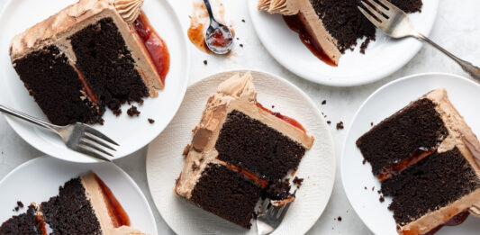 Chocolate PB&J Cake Slices of chocolate layer cake with dark frosting and a red jam filling on white plates, with forks nearby.