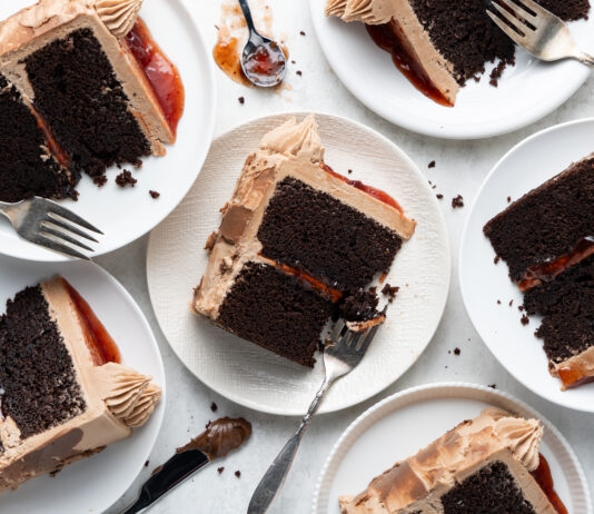 Chocolate PB&J Cake Slices of chocolate layer cake with dark frosting and a red jam filling on white plates, with forks nearby.
