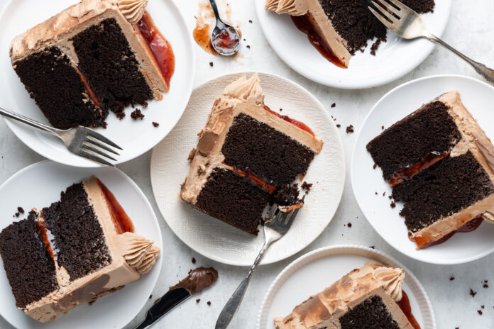 Slices of chocolate layer cake with dark frosting and a red jam filling on white plates, with forks nearby.