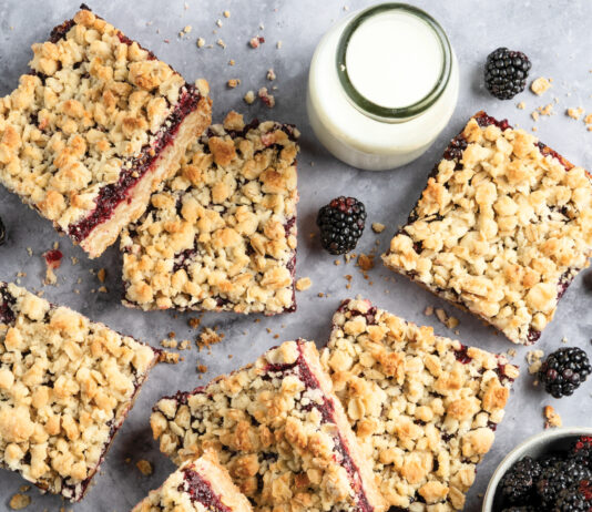 Fast-Fix Baking for Summer Crumbled blackberry bars scattered on a gray surface with a small pitcher of milk and fresh blackberries nearby.