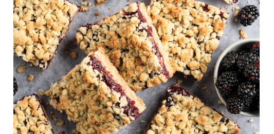 Fast-Fix Baking for Summer Crumbled blackberry bars scattered on a gray surface with a small pitcher of milk and fresh blackberries nearby.