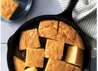 Mayonnaise Cornbread Cast iron skillet filled with golden cornbread squares on a light blue surface, with a striped cloth nearby.