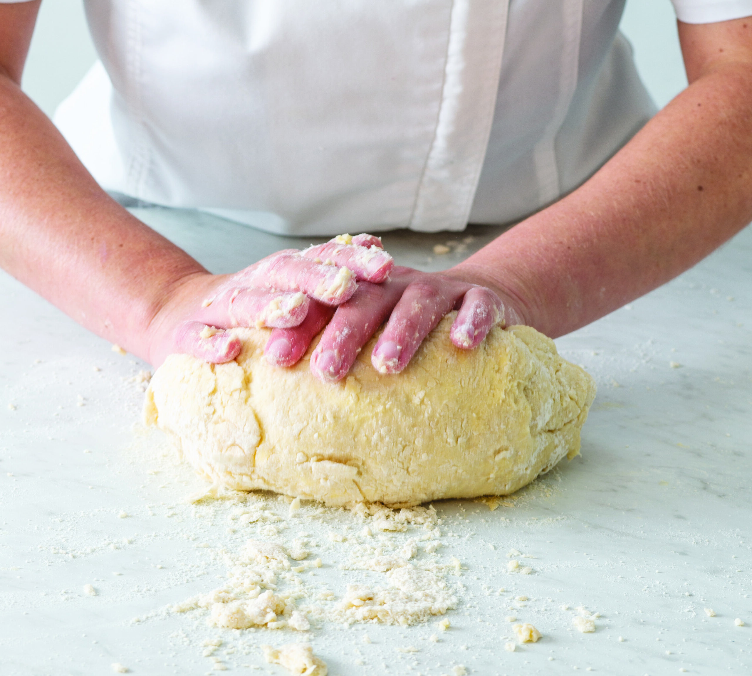 Hands working laminated dough on a floured surface