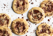 Chunky Chip Cookies Several chocolate chip cookies arranged on white parchment on a light surface, with chocolate crumbs scattered around.
