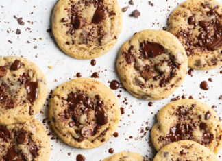 Chunky Chip Cookies Several chocolate chip cookies arranged on white parchment on a light surface, with chocolate crumbs scattered around.