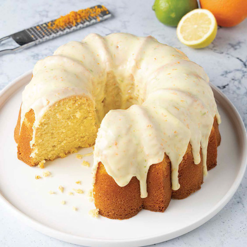 Lemon Bundt cake with white glaze on a white plate; slice removed to reveal moist yellow interior.
