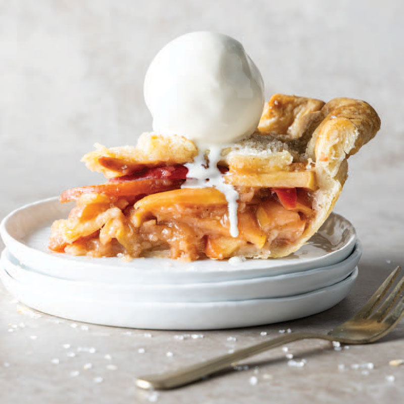 Slice of peach pie with a scoop of vanilla ice cream on top, served on a white plate.