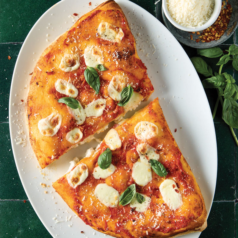 Two triangular slices of tomato‑sauce pizza with mozzarella pearls and fresh basil on a white oval plate.