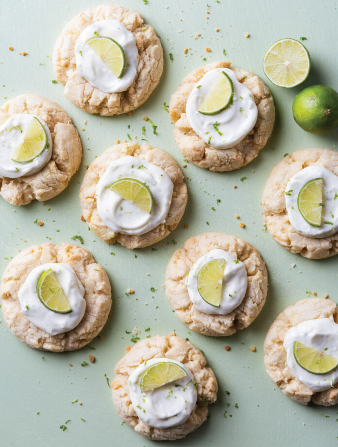 Cakes or cookies topped with white frosting and lime wedges on a pale green background, arranged in a scattered pattern