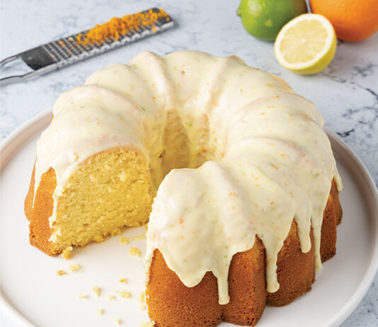 Citrus Pound Cake Lemon Bundt cake with white glaze, sliced to reveal a light yellow crumb; citrus fruits and a grater visible in the background.