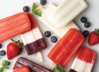 Ice Pops Assorted layered berry popsicles on a white surface, with blueberries, strawberries, and mint garnish nearby.