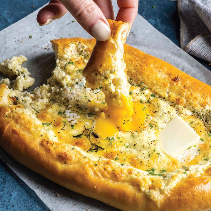 Cheese pizza slice being pulled apart with a runny egg yolk oozing and herbs sprinkled on top.