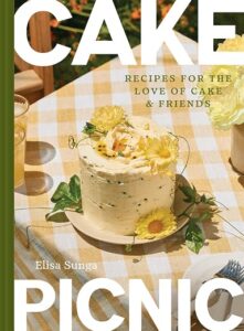 Book cover titled CAKE PICNIC showing a frosted cake on a yellow-checkered picnic table with yellow flowers and greenery, subtitle 'Recipes for the Love of Cake & Friends' by Elisa Sunga.