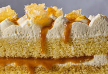 Honey Caramel Layer Cake Close-up of a layered yellow sponge cake with whipped cream, caramel drizzle, and almond shards on top.