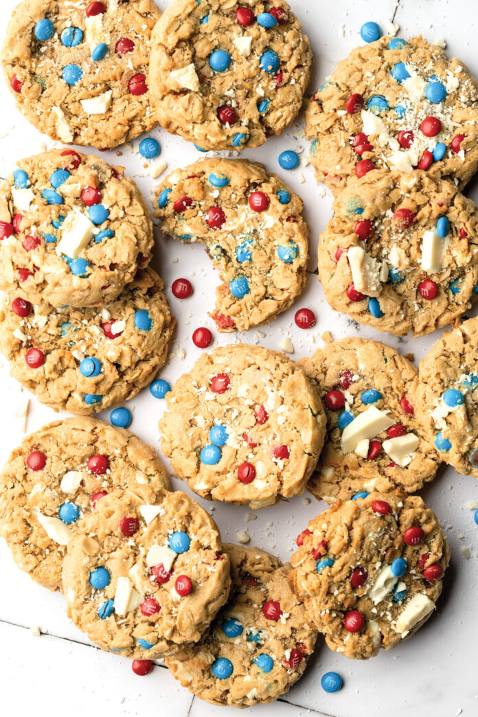 Cookies141SWS Close-up of chunky cookies studded with red and blue M&M candies and white chocolate chunks on a white surface.